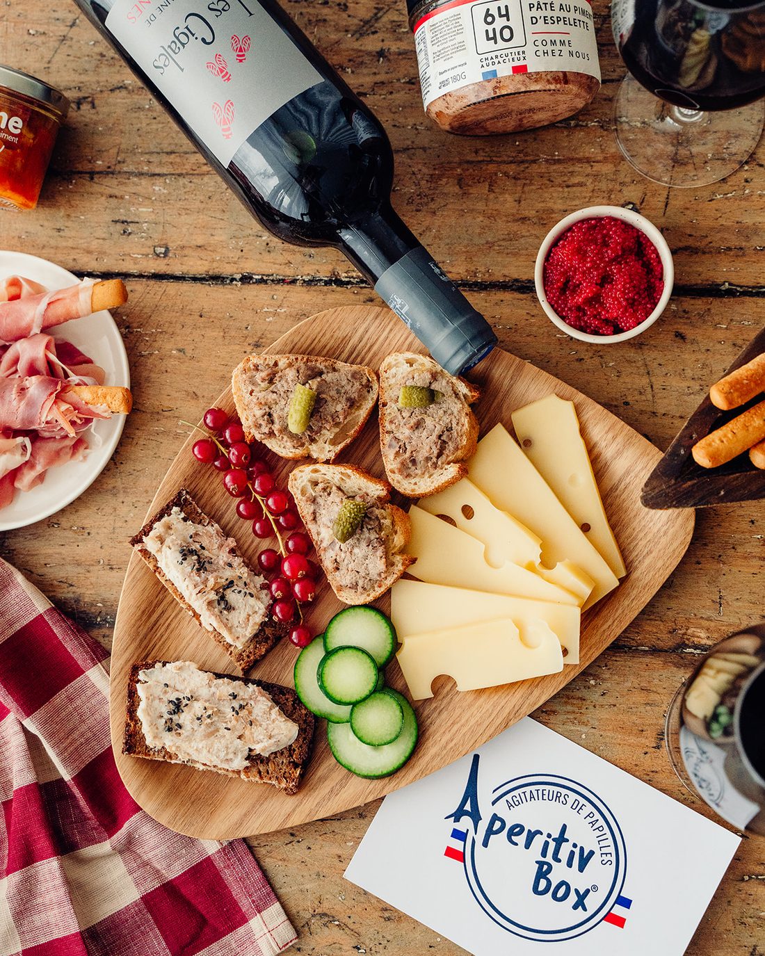 Planche apéritive et bouteille de vin rouge français : pâté, emmental, jambon sec et groseilles